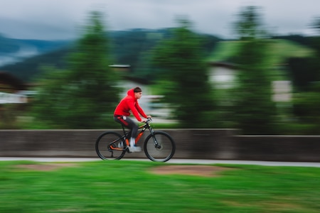 Junge mit roter Kapuzenjacke fährt Mountainbike durch verschwommene Berglandschaft