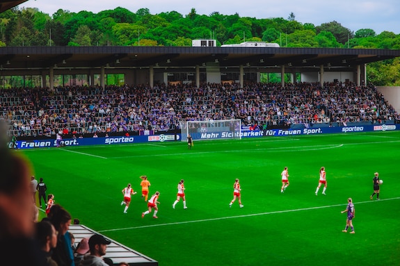 Fußballspiel mit Spielerinnen in Rot und Gelb vor vollen Tribünen in Wien.