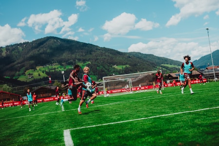 Fußballer trainieren im Trainingslager in den österreichischen Alpen auf einem grünen Rasen mit Bergkulisse.