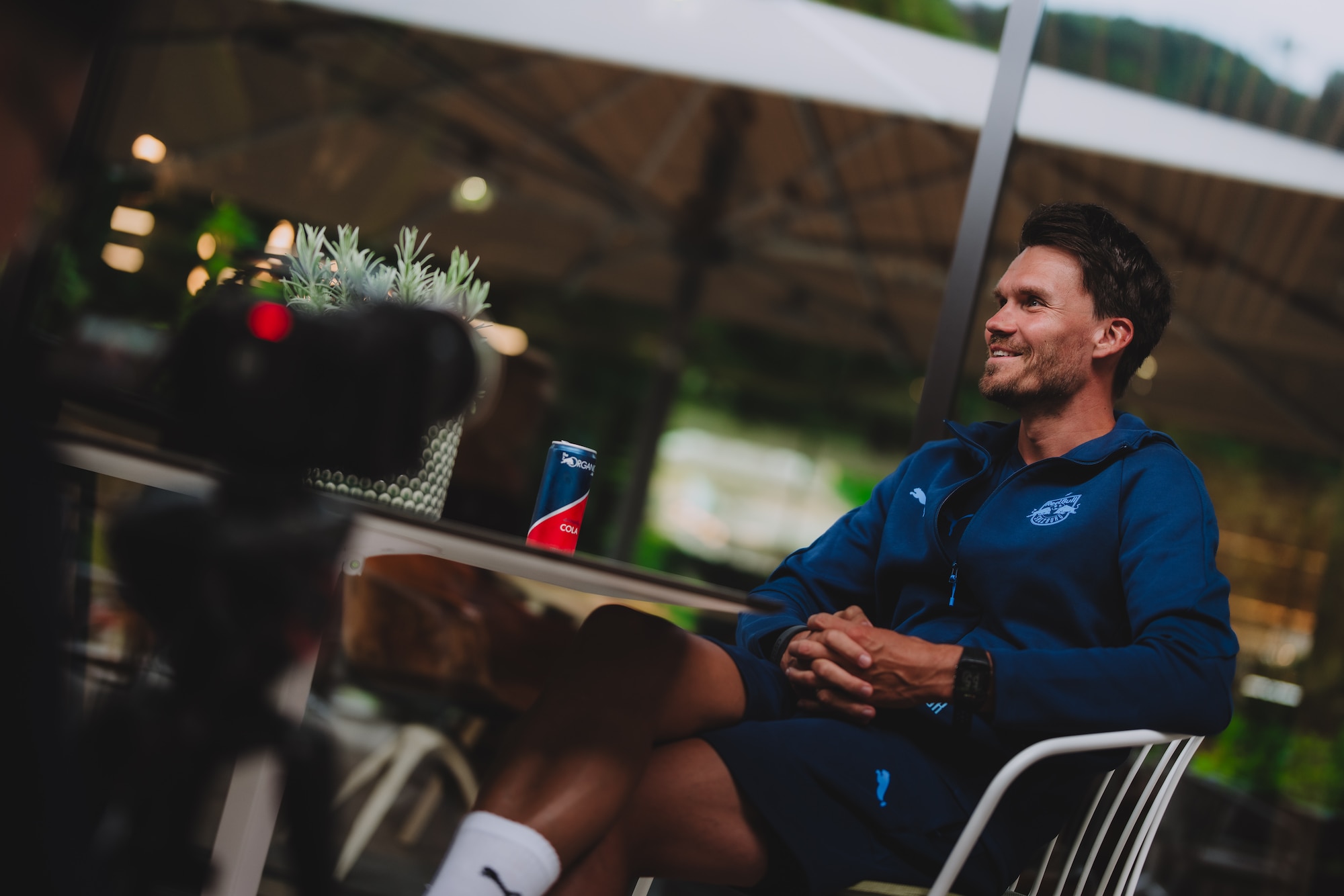Fußballtrainer Matthias Jaissle sitzt im Freien an einem Tisch mit einer Getränkedose.