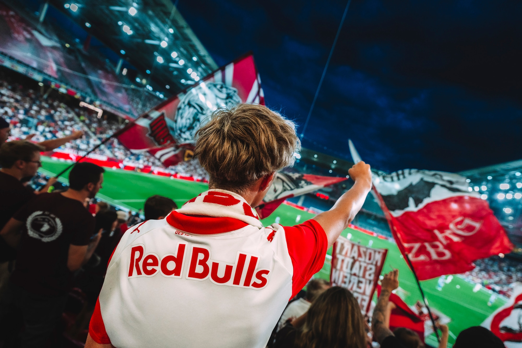 Fußballfans mit Red Bull Trikots und Fahnen im Stadion bei einem Spiel.
