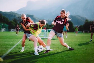 Fußballerinnen im Zweikampf auf einem Rasenplatz in Salzburg mit Bergkulisse.