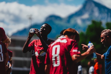 Fußballer trinkt bei Trainingsspiel in Salzburg, Berg im Hintergrund.