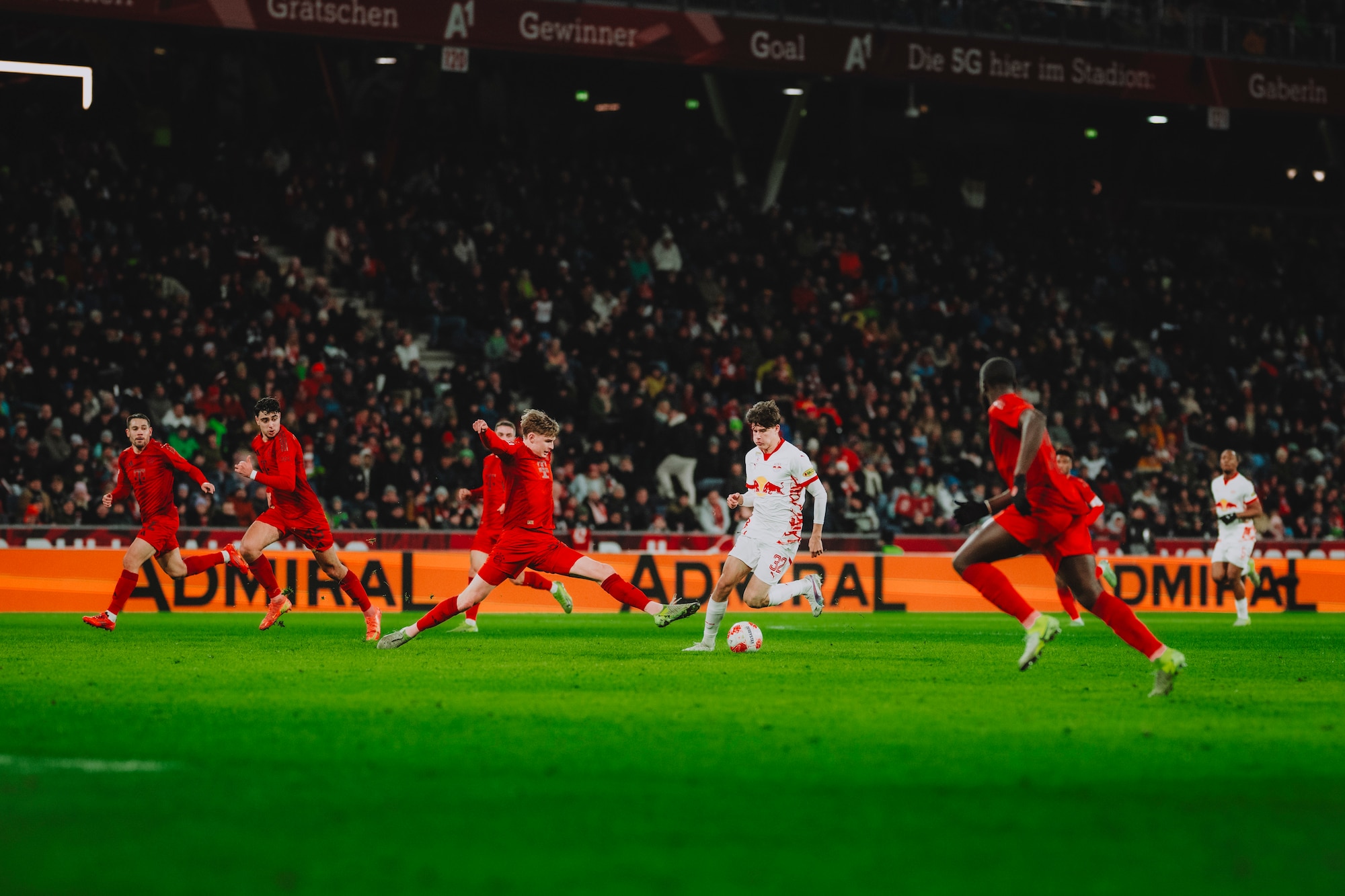 Fußballspieler in Rot und Weiß im Stadion, Admiral-Werbung im Hintergrund