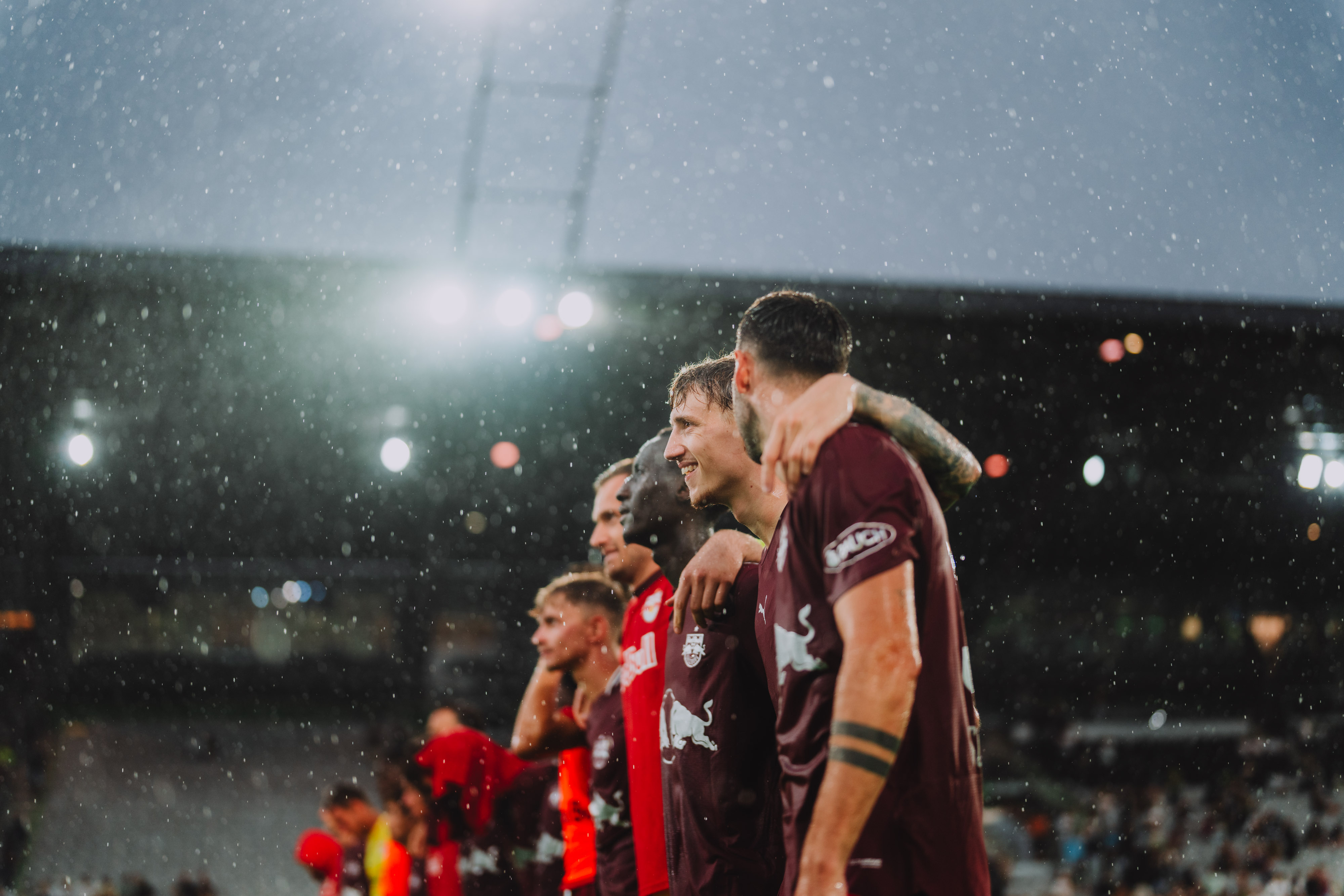 Fußballspieler des FC Salzburg stehen im Regen, Arme um die Schultern gelegt.