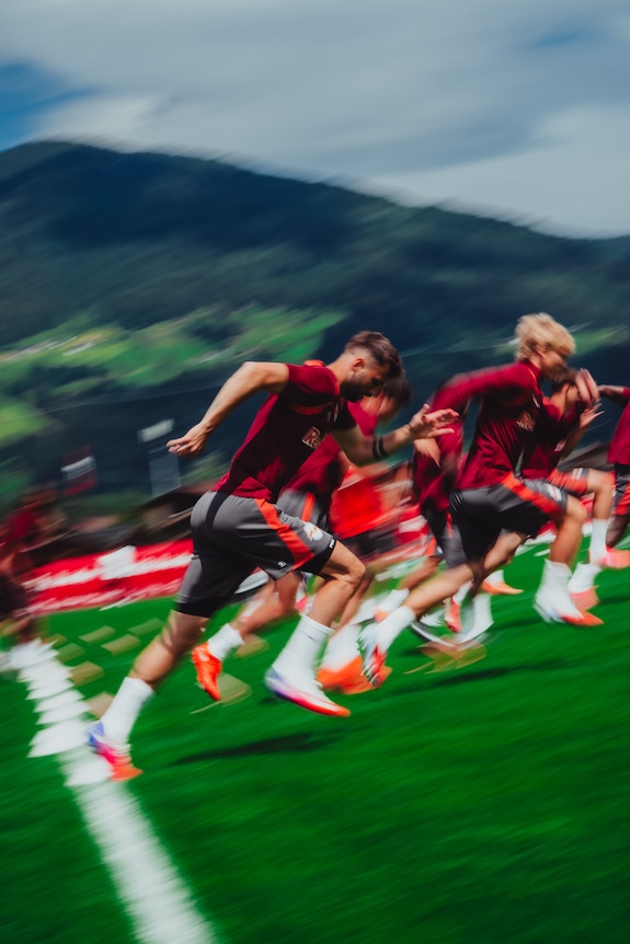 Fußballer im Trainingslager in den Alpen bei Salzburg laufen auf einem grünen Rasen.