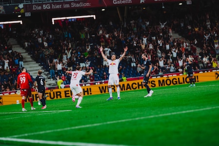 Fußballspieler von RB Salzburg jubeln im Stadion vor Fans, während ein Gegenspieler zusieht.